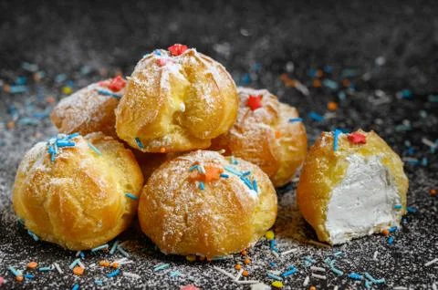 Eclairs on a black background dusted with multicolored sprinkles and powdered Stock Photos