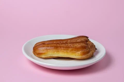 Eclairs on a pink background. One eclair on a white plate.  Stock Photos