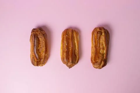 Eclairs on a pink background. Three eclairs lie next to each other. Stock Photos
