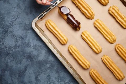 Eclairs, profiterole preparing on baking sheet, spreading chocolate with spoon Stock Photos