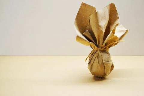 Eco-friendly Easter gift. Egg wrapped in kraft paper stands on light backgrou Stock Photos