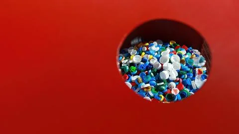 Ecological red bin for plastic bottle caps. The lids are visible inside. Stock Photos