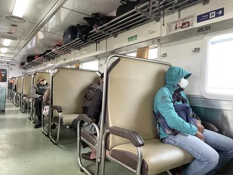 Economy class train interior with two rows of seats with passengers sitting Foto stock