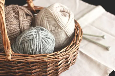 Ecru, brown and grey wool yarn with needles in wooden basket Stock Photos