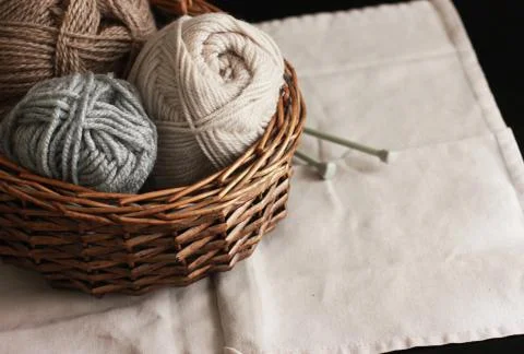 Ecru, brown and grey wool yarn with needles in wooden basket Stock Photos