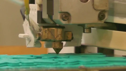 ECU of the head of a 3D printer; camera zooms out to medium close up. Stock Footage 75346368
