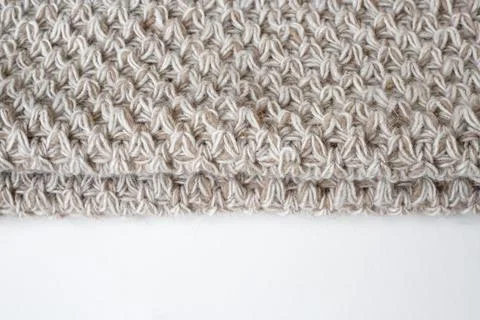 Edge of a beige crocheted wool blanket on a white background. Stock Photos