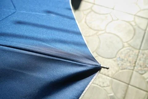 Edge of a blue umbrella with shadow over a blurred tile floor Stock Photos
