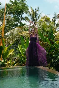 On the edge of the pool against the palm tree stands a girl in a long evening Stock Photos
