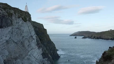 From the edge of a steep rocky precipice, a pristine white lighthouse Stock Footage 253581673