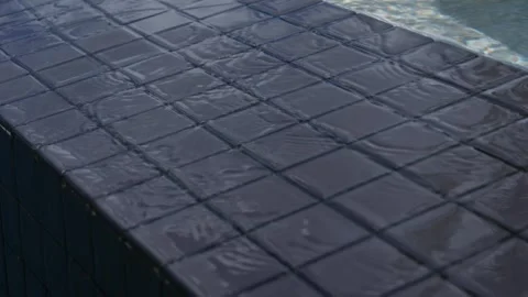 Edge of swimming pool. Edge covered with dark square tiles that is wet. Water in Stock Footage 297751657