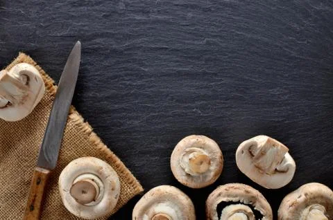 Edible half pieced mushrooms - champignons and rustic knife on vintage slate Stock Photos
