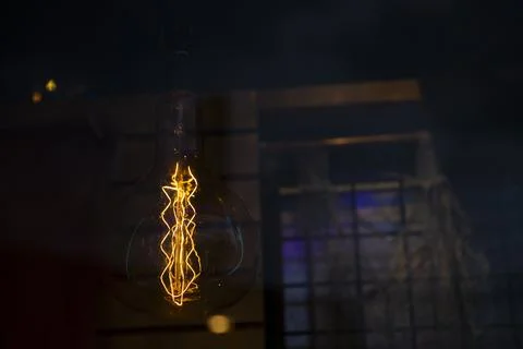 Edison globe shaped light bulb visible orange filaments over a dark backgroun Foto stock