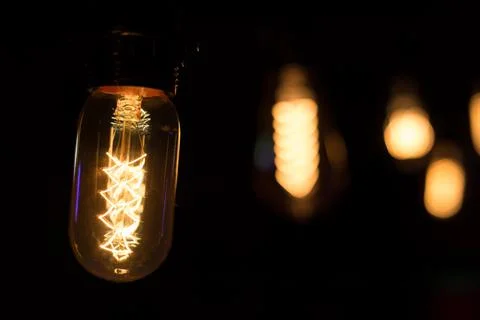 Edison lamp with warm light sways lightly on a black background Stock Photos