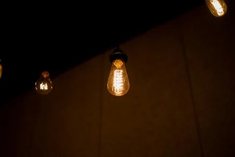 Edison lamp with warm light sways lightly on a black background Stock Photos