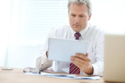 Editing my digital document. Mature businessman holding a tablet while sitting Stock Photos