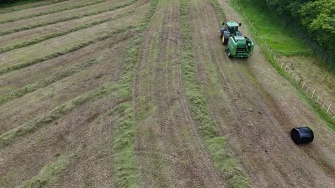 Editorial: A baling machine drops out a newly wrapped haylage bale aerial Stock Footage 294684955