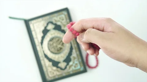 EDITORIAL: HAND COUNTING TASBIH OR ROSARY BEADS WITH HOLY QURAN IN BACKGROUND. Video stock 107140914