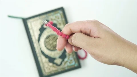 EDITORIAL: HAND COUNTING TASBIH OR ROSARY BEADS WITH HOLY QURAN IN BACKGROUND. Video stock 107140954