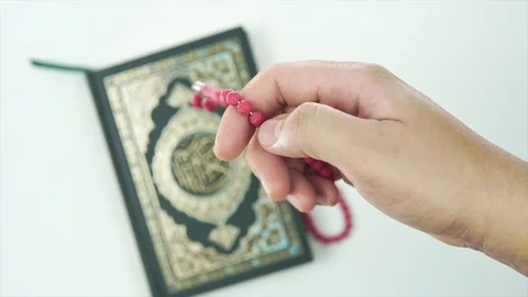 EDITORIAL: HAND COUNTING TASBIH OR ROSARY BEADS WITH HOLY QURAN IN BACKGROUND. Video stock 107141012