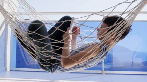Education, distance learning. Kid doing homework in hammock on balcony Stock Footage 128570605