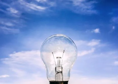Eelectrical light bulb in hand on blue sky background. Hand holding light bul Stock Photos