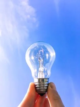 Eelectrical light bulb in hand on blue sky background. Hand holding light bul Stock Photos