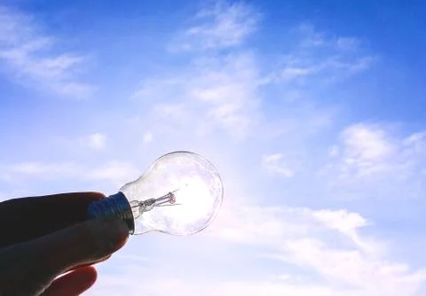Eelectrical light bulb in hand on blue sky background. Hand holding light bul Foto stock