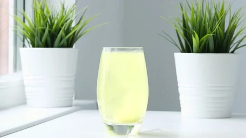 Effervescent pill falling down in glass and colors water yellow. Real time Video stock 220595659
