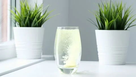 Effervescent pill falling down in glass and colors water yellow. Slow motion Video stock 232279294