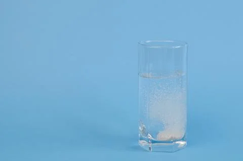 An effervescent tablet that dissolves and fizzes in a glass of water on a blue Stock Photos