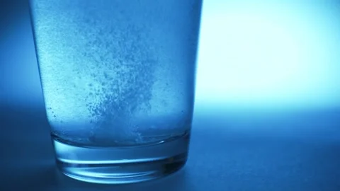 An effervescent tablet dissolves at the bottom of a glass of water Stock Footage 148457778
