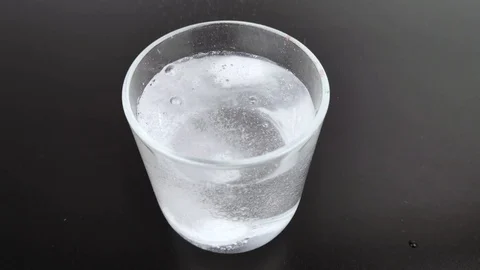 An effervescent tablet dissolves in a glass emitting a lot of bubbles. Macro vid Stock Footage 125393439