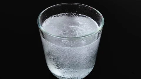 An effervescent tablet dissolves in a glass emitting a lot of bubbles. Macro vid Stock Footage 125393498
