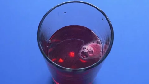 An effervescent tablet dissolves in a glass of water which turns burgundy, .. Stock Footage 283390844