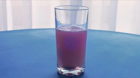 An effervescent tablet dissolves in a glass of water which turns red. Mediu.. Vidéo 284750551
