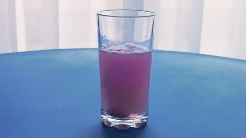 An effervescent tablet dissolves in a glass of water which turns red. Mediu.. 库存影片 288737998