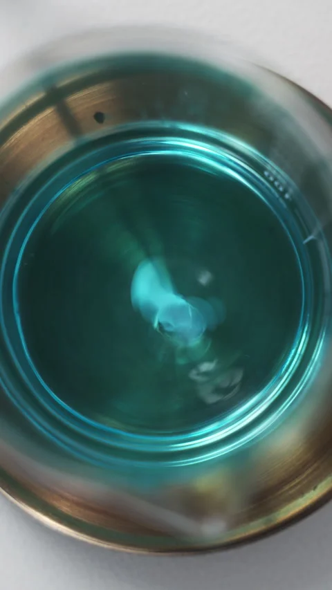 Effervescent tablet dissolving in blue liquid creating a vortex inside a metal Stock Footage 333795076