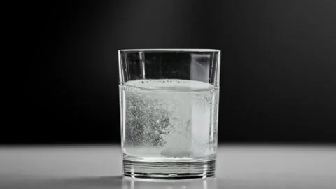 Effervescent Tablet Falling into Fresh Water in Glass Cup Making Healthy Drink Stock Footage 240557042
