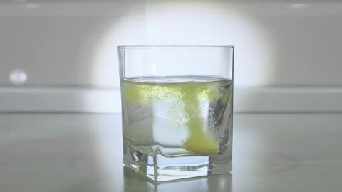 Effervescent yellow tablet dissolves in a glass of water Stock Footage 271070417