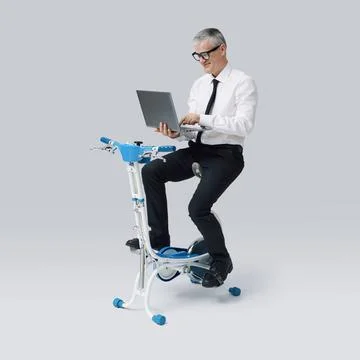 Efficient business executive working out on a spinning bike and working Stock Photos