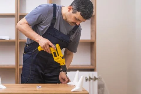 Efficient handyman in uniform assembling a wooden rack with precision and skill Stock Photos