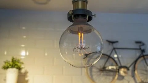 Efficient incandescent light bulb waste electricity against a tiled wall with a Stock Photos