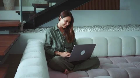 Efficient remote work setup young adult lady is seen sitting on couch at home Stock Footage 312507340