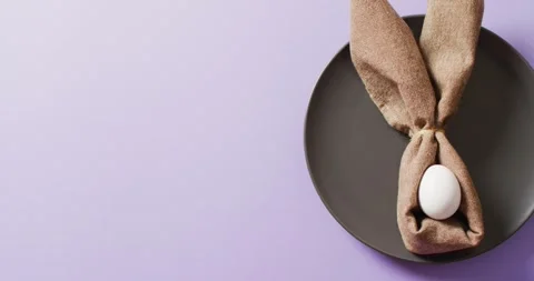 Egg and ribbon in shape of rabbit on plate on purple background with copy space Stock Footage 331307174