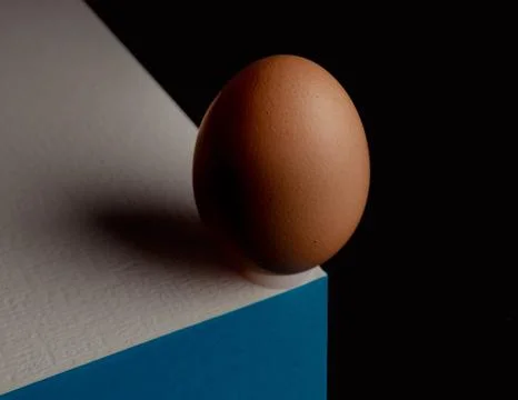 Egg, balancing on table edge. Minimalistic egg stands on colorful table. Stock Photos