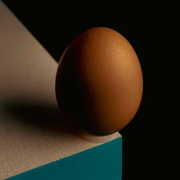 Egg, balancing on table edge. Minimalistic egg stands on colorful table. Stock Photos