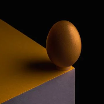 Egg, balancing on table edge. Minimalistic egg stands on colorful table Stock Photos