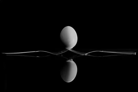 An egg balancing on two forks. Reflection on a black background. Stock Photos
