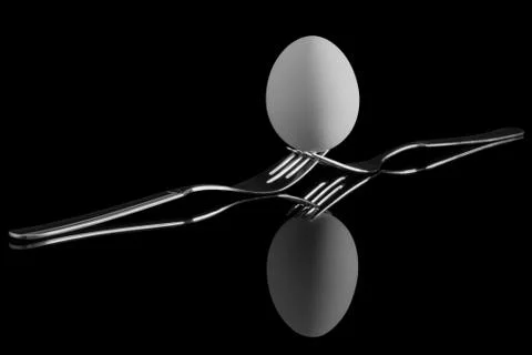 An egg balancing on two forks. Reflection on a black background. Stock Photos